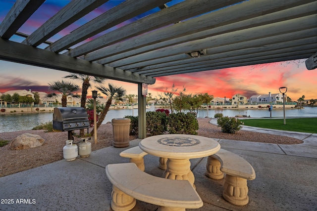 patio terrace at dusk with a water view, grilling area, and a pergola