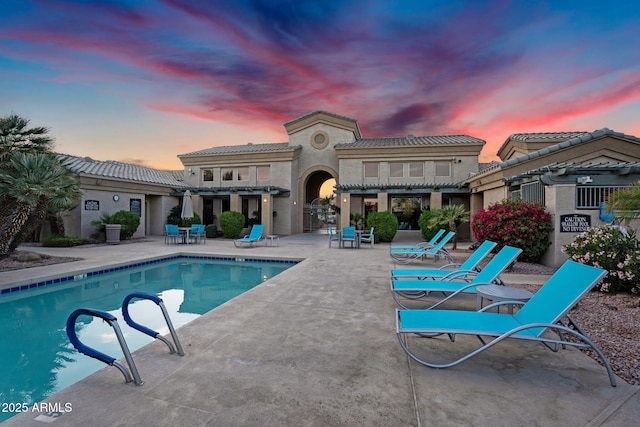 pool at dusk featuring an outdoor pool and a patio