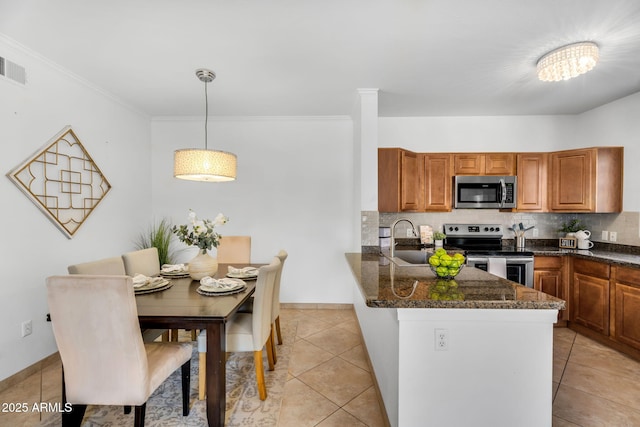 kitchen featuring brown cabinets, decorative backsplash, appliances with stainless steel finishes, a sink, and a peninsula