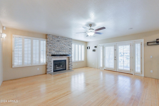 unfurnished living room with a stone fireplace, light hardwood / wood-style flooring, and a healthy amount of sunlight