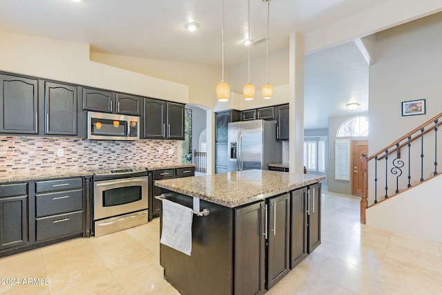 kitchen with appliances with stainless steel finishes, hanging light fixtures, decorative backsplash, vaulted ceiling, and light stone counters