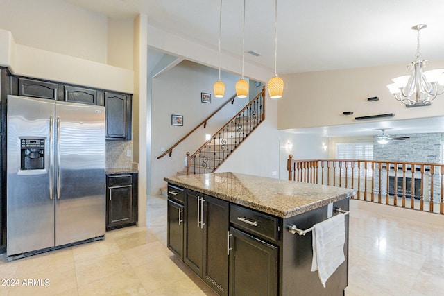 kitchen featuring light stone countertops, hanging light fixtures, stainless steel fridge with ice dispenser, a center island, and ceiling fan with notable chandelier