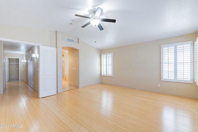 empty room featuring ceiling fan, vaulted ceiling, light hardwood / wood-style floors, and a healthy amount of sunlight