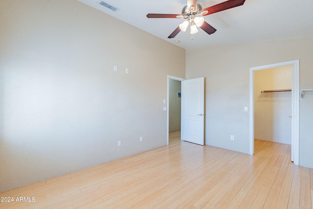 unfurnished bedroom featuring light wood-type flooring, a closet, lofted ceiling, a walk in closet, and ceiling fan