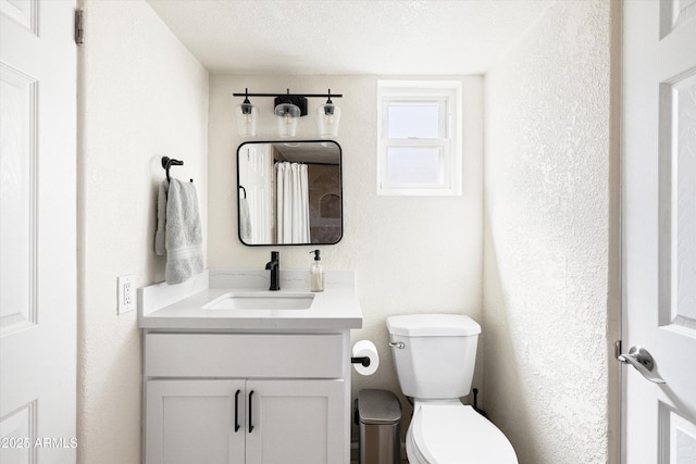 bathroom featuring toilet, vanity, a textured wall, and a textured ceiling