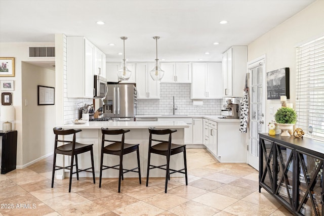 kitchen with stainless steel appliances, a peninsula, light countertops, and backsplash