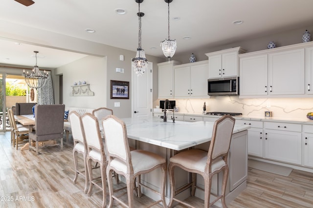 kitchen featuring hanging light fixtures, an island with sink, white cabinets, and appliances with stainless steel finishes