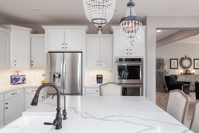 kitchen with an inviting chandelier, a kitchen breakfast bar, pendant lighting, stainless steel appliances, and white cabinets