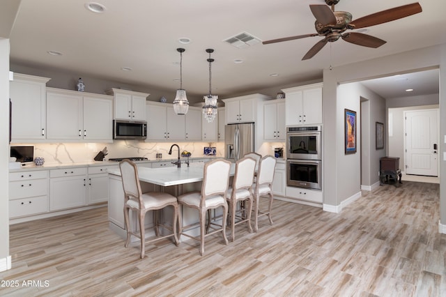 kitchen featuring a kitchen bar, white cabinetry, hanging light fixtures, appliances with stainless steel finishes, and a kitchen island with sink