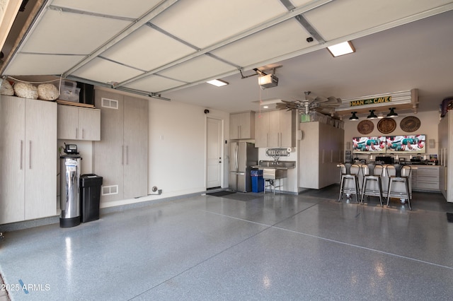 garage with a garage door opener, stainless steel fridge, and sink