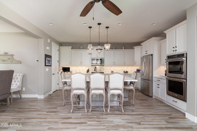 kitchen with white cabinetry, decorative light fixtures, a center island with sink, a kitchen breakfast bar, and stainless steel appliances