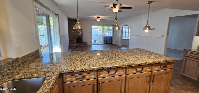 kitchen featuring lofted ceiling, decorative light fixtures, a fireplace, and stone counters