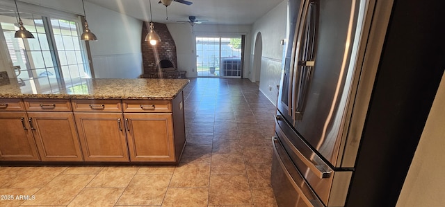 kitchen featuring light stone counters, a brick fireplace, stainless steel refrigerator, pendant lighting, and ceiling fan