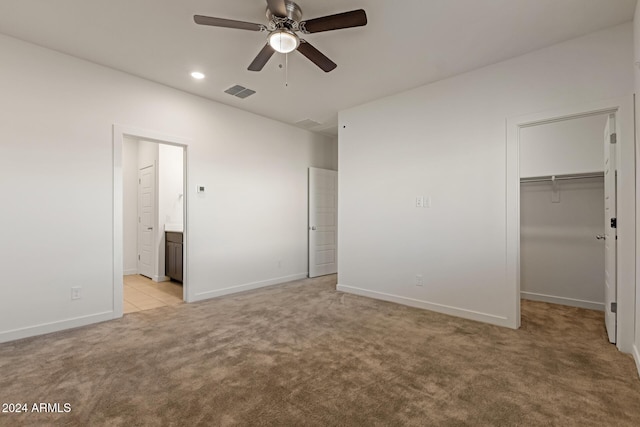 unfurnished bedroom with ensuite bathroom, ceiling fan, a spacious closet, light colored carpet, and a closet