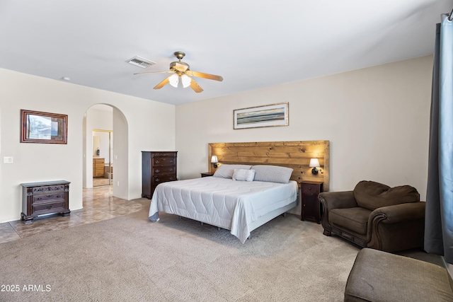 bedroom with arched walkways, ensuite bath, light carpet, ceiling fan, and visible vents
