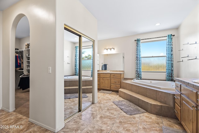 full bathroom with two vanities, a healthy amount of sunlight, a garden tub, and a walk in closet