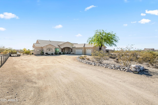 view of front of home with fence, dirt driveway, stucco siding, and an attached garage