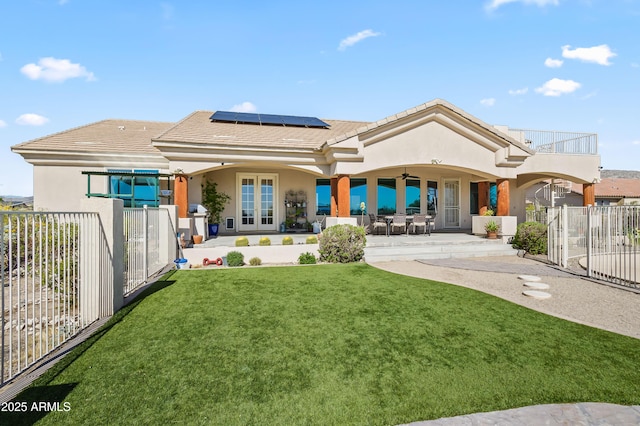back of property with a yard, fence private yard, a patio, roof mounted solar panels, and a ceiling fan