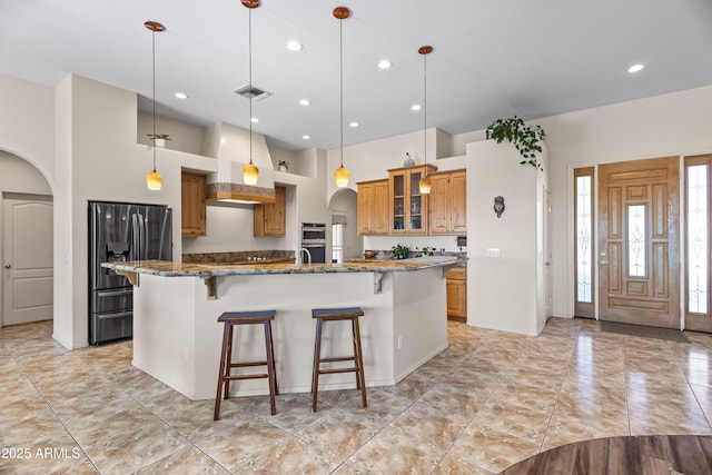 kitchen featuring a kitchen breakfast bar, visible vents, stainless steel appliances, arched walkways, and custom exhaust hood