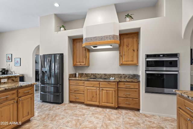 kitchen featuring premium range hood, arched walkways, light stone counters, and stainless steel appliances