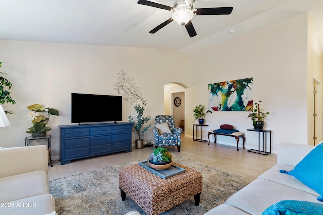 living area featuring ceiling fan, arched walkways, baseboards, wood finished floors, and lofted ceiling