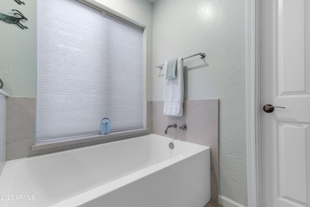 full bath featuring a textured wall and a bath
