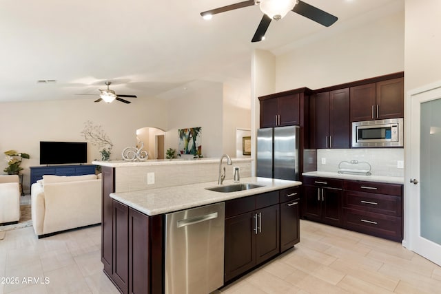 kitchen featuring ceiling fan, a sink, stainless steel appliances, open floor plan, and tasteful backsplash