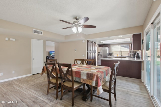 dining space featuring visible vents, light wood-style flooring, a textured ceiling, baseboards, and ceiling fan