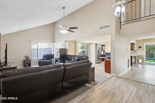 living area with a wealth of natural light, ceiling fan with notable chandelier, visible vents, and light wood finished floors