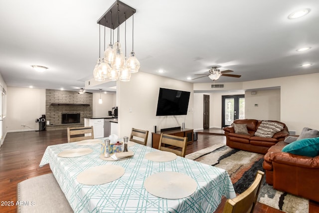 dining area featuring ceiling fan, a brick fireplace, visible vents, and dark wood-style floors