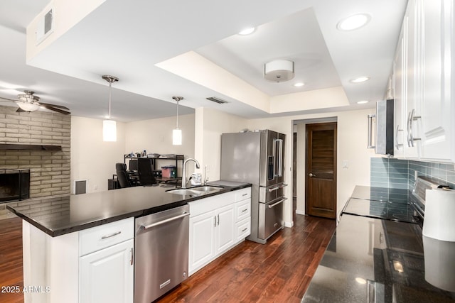 kitchen with a sink, stainless steel appliances, white cabinetry, a raised ceiling, and dark countertops