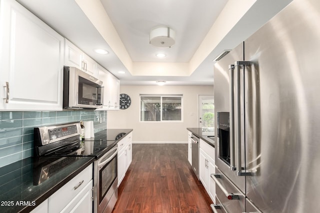 kitchen featuring stainless steel appliances, baseboards, a raised ceiling, tasteful backsplash, and dark wood-style floors