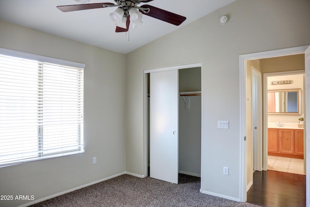 unfurnished bedroom featuring ceiling fan, carpet, vaulted ceiling, sink, and a closet