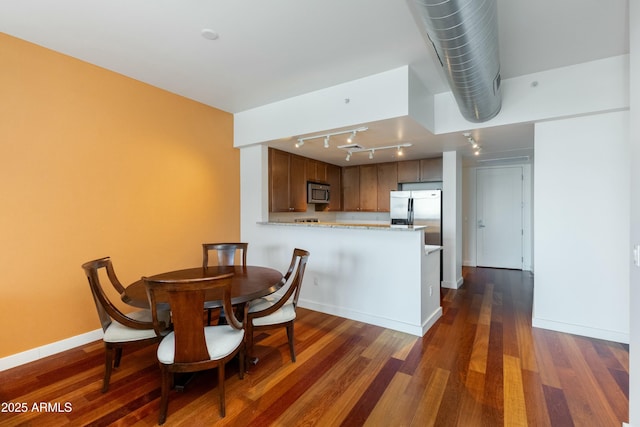 dining room featuring rail lighting, baseboards, and dark wood finished floors