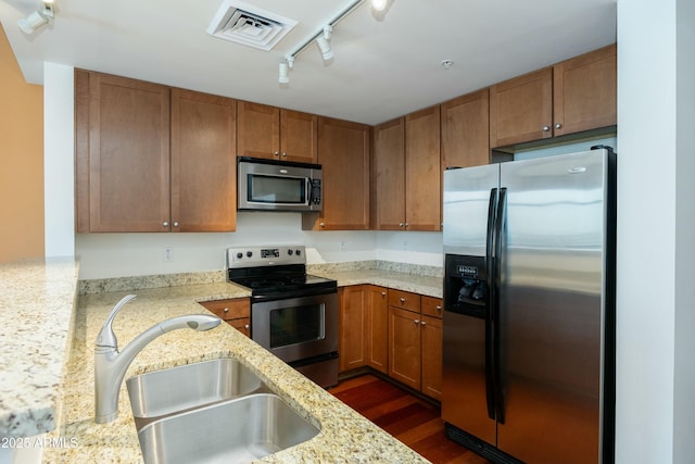 kitchen with visible vents, a sink, appliances with stainless steel finishes, brown cabinetry, and rail lighting