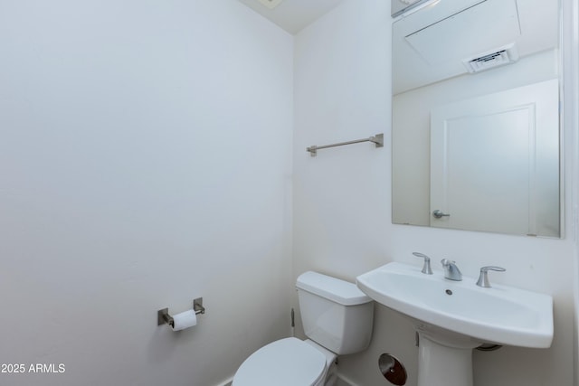 half bath with toilet, a sink, and visible vents