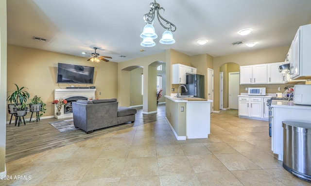 kitchen with black refrigerator, ceiling fan with notable chandelier, sink, decorative light fixtures, and white cabinets