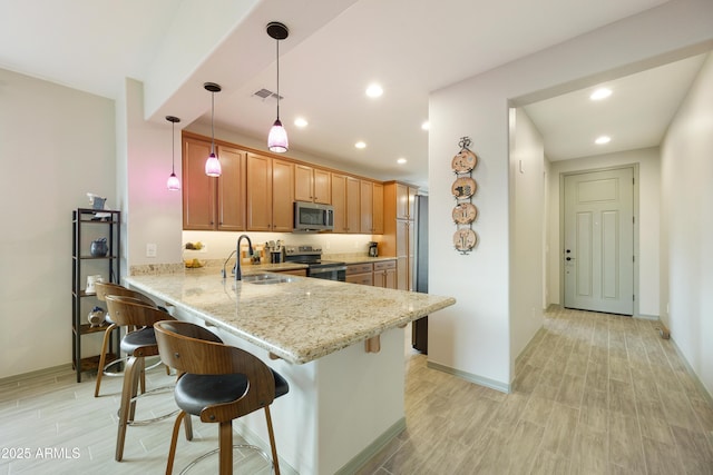 kitchen with a breakfast bar, sink, decorative light fixtures, appliances with stainless steel finishes, and kitchen peninsula