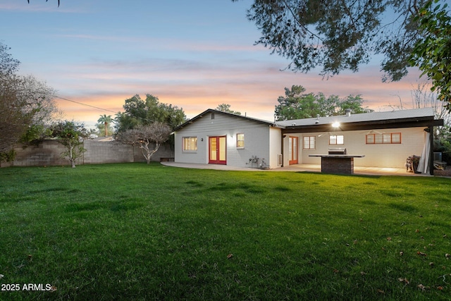 back of property at dusk featuring a patio, french doors, a lawn, and fence