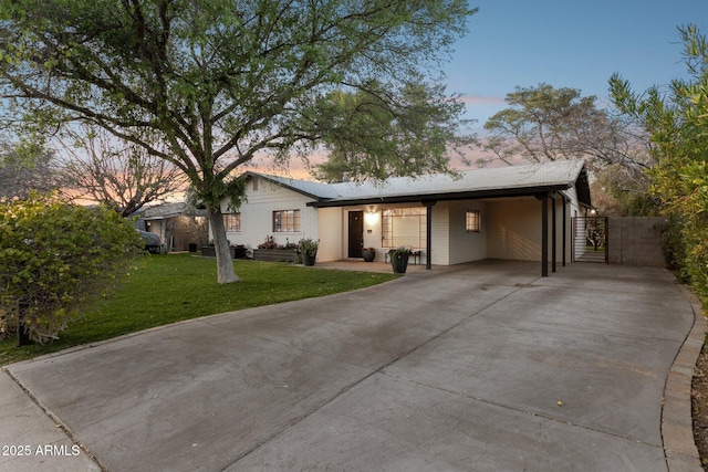 ranch-style house featuring a front yard, concrete driveway, an attached carport, and a gate