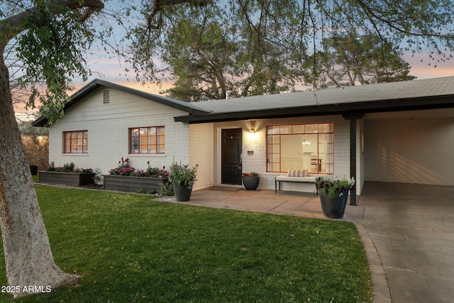 back of property at dusk featuring brick siding and a yard