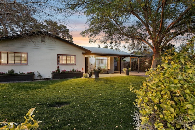 back of property at dusk featuring a patio area, a lawn, and brick siding
