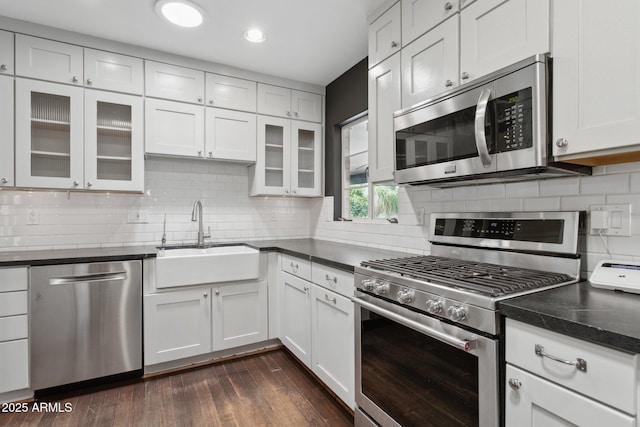 kitchen with appliances with stainless steel finishes, dark wood-style flooring, a sink, and decorative backsplash