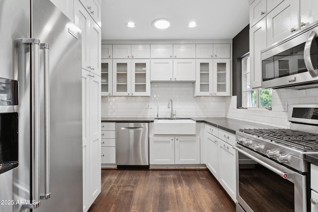 kitchen featuring stainless steel appliances, dark countertops, a sink, and glass insert cabinets