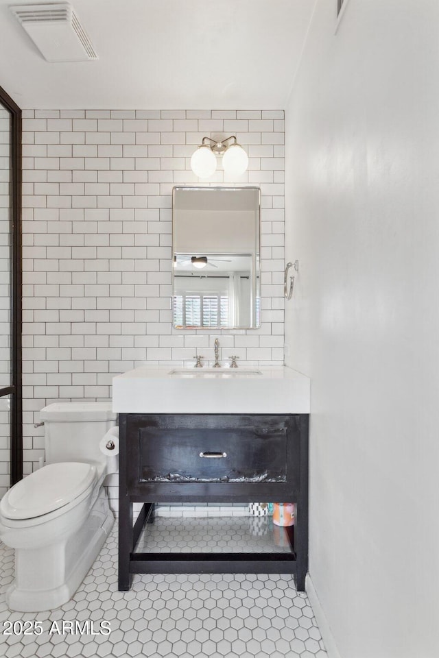 half bath featuring toilet, tile walls, vanity, visible vents, and tile patterned floors