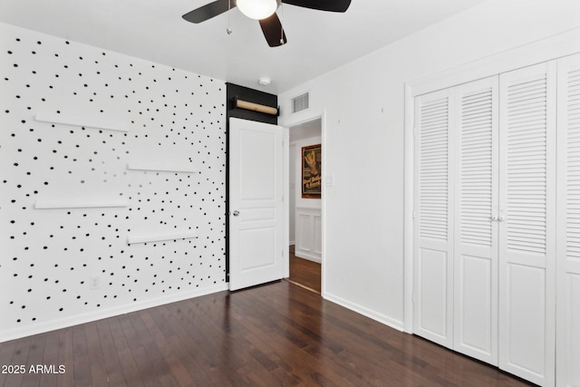 unfurnished bedroom with dark wood finished floors, a closet, visible vents, baseboards, and wallpapered walls