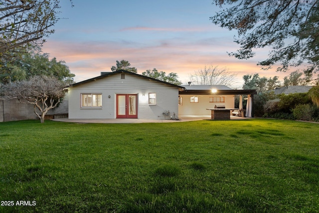 back of house at dusk with a yard, fence, french doors, and a patio
