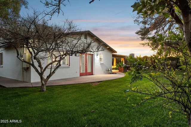back of property at dusk featuring brick siding, a lawn, a patio, and french doors