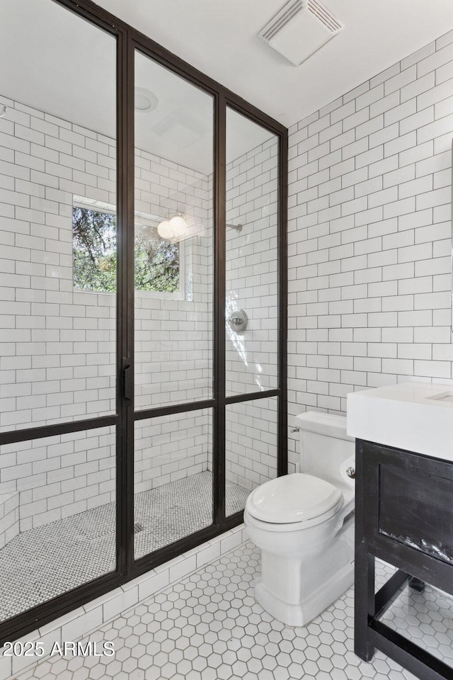 full bath featuring tile walls, visible vents, toilet, a stall shower, and tile patterned flooring