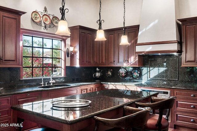 kitchen with decorative light fixtures, dark stone countertops, custom exhaust hood, and sink